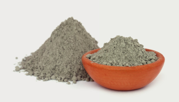 Two piles of medium grey tin powder, one in a pile in the background and one in an terracotta colored bowl.
