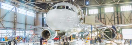 A commercial airliner sits in a maintenance hanger with multiple wires and scaffolds surrounding it.