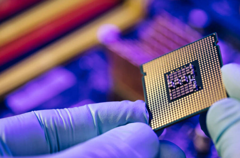 A semiconductor chip being held in hands that are covered with light blue latex gloves.